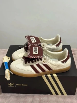 Adidas Wales Bonner  - Unika sneakers från Adidas x Wales Bonner i krämvitt och vinrött med klassiska tre ränder på sidan. Ovandelen har en mix av läder och hårig textur, kontrastsömmar och gummisula. Extra skosnören medföljer. Perfekt för dig som vill sticka ut med din stil. Passar både killar o tjejer är väldigt efterfrågad o snygga