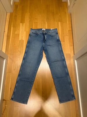 Blå raka jeans från Wrangler - Säljer ett par klassiska blå jeans från Wrangler, modell Redding. Jeansen har rak passform, fem fickor och snygga kontrastsömmar. Tillverkade i slitstark denim med dragkedjegylf. Perfekta för en avslappnad och tidlös stil.                                        Modellen är 185cm lång och väger 82kg.