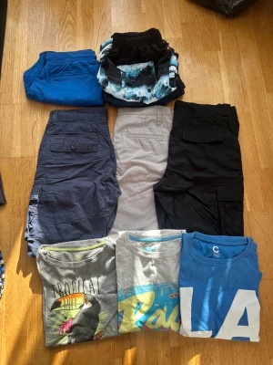 Flera shorts i olika färger och stilar - Säljer ett gäng shorts i olika färger och modeller. Här finns blå, svarta, grå och mönstrade shorts, vissa med fickor på sidorna och andra i sportig stil. 3 st T-shirt 3 badbyxor 1 mjukisbyxa Perfekta för sommaren och avslappnade dagar.  Stl 158 barn