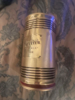 Jean Paul Gaultier Le Male Elixir - Säljer en Jean Paul Gaultier Le Male Elixir parfym. Flaskan har en unik design i form av en manlig torso i guld med svarta ränder. Kommer i en guldfärgad metallburk med märkets logga. Perfekt för dig som gillar exklusiva och ikoniska dofter. Ungefär hälften kvar