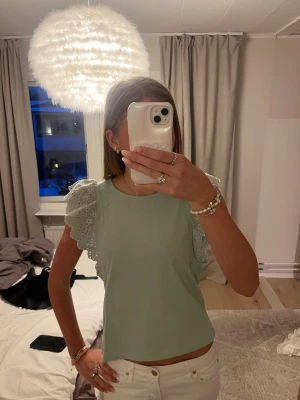 Ljusgrön blus med spetsärmar - Supersöt ljusgrön blus med volangiga spetsärmar och rund hals. Toppen har en croppad passform och är perfekt för dig som gillar romantiska detaljer. Materialet känns som bomull och spetsen ger en extra feminin touch.