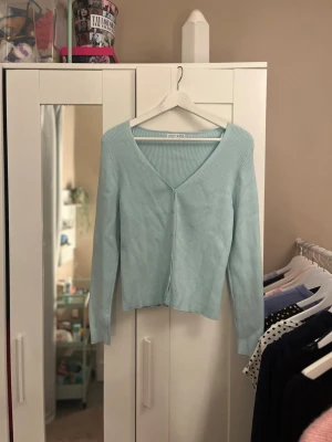 Ljusblå ribbad kofta - Snygg ljusblå ribbad kofta från Primark med djup V-ringning och lång ärm. Koftan har en croppad passform och är tillverkad i ett mjukt, stretchigt material som sitter skönt på kroppen. Perfekt att styla med jeans eller kjol.