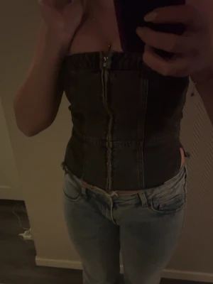 Svart denim korsettopp från Zara - Säljer en svart/grå jeans tubtopp med dragkedja, och slits. Jätte fin och aldrig använt och är ifrån Zara i storlek S. PRIS KAN DISKUTERAS!💞