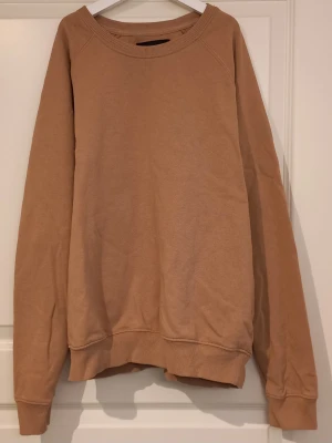 Beige sweatshirt från 157 - En enkel och snygg beige sweatshirt från 157 i storlek M. Tröjan har rund hals, långa ärmar och ribbade muddar vid ärmslut och nederkant. Perfekt för en chill och avslappnad stil.