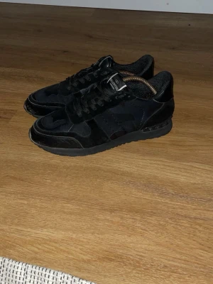 Valentino rockrunners  - Säljer ett par helsvarta sneakers från Valentino med coola detaljer och logga på plösen. Skorna har en mix av mocka och läder, samt en unik stjärnformad patch på tån. Klassisk låg modell med snörning och bekväm sula. Lite små defekter men fortfarande riktigt snygga. Hör gärna av er vid prisförslag eller funderingar😊