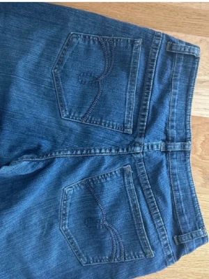 Blå bootcut jeans från Crocker - Säljer ett par klassiska blå bootcut jeans från Crocker. Snygga sömmar på bakfickorna och är gjorda i slitstark denim. Perfekta för dig som gillar en retro vibe och vill ha ett par jeans med lite vidare ben. 2000-tals jeans.