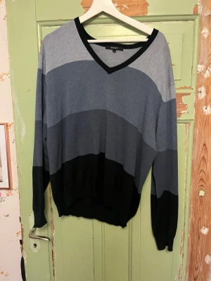 Randig tröja med V-ringning från Gant - Snygg tröja från Gant med breda horisontella ränder i olika nyanser av grått och svart. Tröjan har V-ringning med svart kant, långa ärmar och ribbade muddar. Perfekt för en avslappnad och stilren look. Priset kan alltid diskuteras och be gärna om bilder!