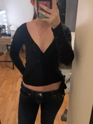 Svart croppad omlottopp - Svart croppad omlottopp med v-ringning och långa ärmar. Tunn och stretchig, vilket gör den bekväm att bära.