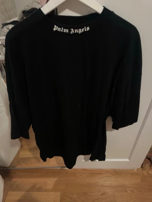 Svart Palm Angels t-shirt - Svart oversized t-shirt från Palm Angels med stort vitt logotryck på ryggen och mindre logga vid halsen fram. Klassisk rund hals och korta ärmar. Perfekt för dig som gillar streetwear och vill sticka ut med en ikonisk look.