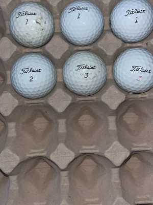 6 stycken Titleist golfbollar Pro V1 - Säljer ett gäng vita golfbollar från Titleist, modell Pro V1. Bollarna har klassisk dimple-yta och är märkta med både svart och rosa text. Perfekta för dig som vill fylla på golfbagen med kvalitetsbollar.