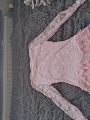 Rosa spetsklänning med volanger - Supersöt rosa kortklänning i spets med långa ärmar och flera lager volanger nedtill. Klänningen har en feminin och romantisk look.Materialet är spets och klänningen är figurnära upptill. Helt ny aldrig använd då den var för liten