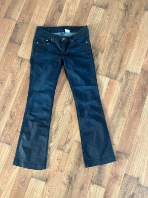 Jeans från H&M - Snygga mörkblå bootcut jeans från H&M med klassisk femficksmodell och guldfärgade nitar. Jeansen har låg midja och utsvängda ben, perfekta för en trendig och avslappnad look. 29/30 men små i storlek