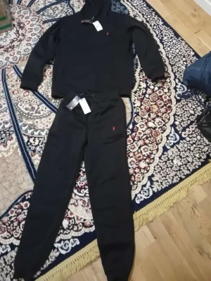 Svarta mjukisbyxor från Polo Ralph Lauren - Säljer ett par svarta mjukisbyxor från Polo Ralph Lauren med dragsko i midjan och resår vid bensluten. Byxorna har en liten röd logga broderad på ena benet. Perfekta för chill dagar och riktigt sköna att ha på sig.