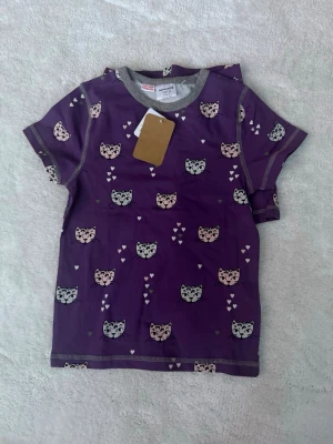 Lila pyjamas med kattmönster Maxomorra - Söt lila pyjamas från Maxomorra med korta ärmar och grå kant vid hals och ärmslut. Pyjamasen har ett gulligt kattmönster i svart, vitt och rosa samt små hjärtan. Tillverkad i ekologisk bomull för extra mjuk känsla. Ordinarie pris 499 kr 