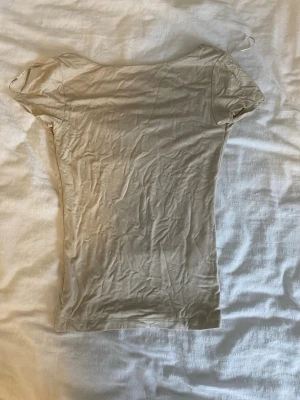 Beige tight t-shirt med öppen rygg - En enkel och stilren beige t-shirt med tight passform och korta ärmar. Toppen har en öppen, rundad rygg. Knappt använd, som ny.