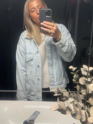 Ljusblå oversized jeansjacka - Säljer en ljusblå oversized jeansjacka med klassisk krage och knappstängning framtill. Jackan har två bröstfickor med lock och knappar samt raka ärmar. Perfekt för en avslappnad och trendig look.