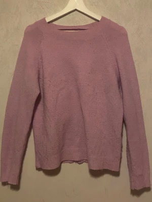 Rosa stickad tröja Vero Moda - Mysig rosa stickad tröja från Vero Moda med rund halsringning och långa ärmar. Tröjan har ribbade muddar vid ärmslut och nederkant, och är tillverkad i ett mjukt material som passar perfekt för kyligare dagar.