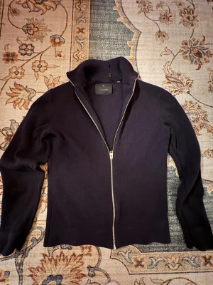 Mörkblå stickad ziptröja - Säljer en mörkblå stickad ziptröja med dragkedja framtill och långa ärmar. Tröjan har en enkel, stilren design och passar perfekt till jeans eller över en t-shirt. Materialet är mjukt och bekvämt ut, perfekt för kyligare dagar. Storlek Xs men passar också som S