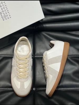 Maison Margiela - Stilrena sneakers från Maison Margiela i vitt och beige med ovandel i läder och mocka, samt klassisk gummisula i brunt och snygga ton-i-ton snören. Perfekta för dig som gillar minimalistisk och clean stil.