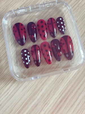 Press-on naglar med nyckelpigemotiv - Snygga press-on naglar i mandelform med handmålat nyckelpigemotiv. Färgerna är röd och svart med vita detaljer och prickar. Naglarna kommer i ett set om tio och är tillverkade i plast. Perfekt för dig som vill ha en lekfull och unik nageldesign. 10st naglar!!