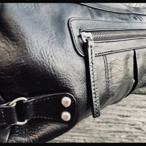 Clutch i skinn från Wera! - Stor svart clutch i skinn med flera fack, dragkedja och snygga detaljer från Wera. Mått: 35 x 20 cm. Jättebra skick!