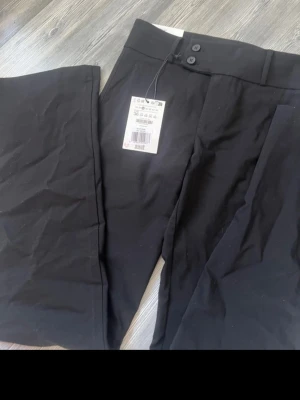 Populära Svarta kostymbyxor från Bershka - Snygga svarta kostymbyxor från Bershka med raka ben. Byxorna har två knappar i midjan och är tillverkade i ett mjukt, vävt material som ger en clean look. Perfekta för en stilren outfit.