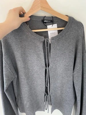 Grå kofta med knytning från Gina Tricot - Snygg grå kofta från Gina Tricot med knytning framtill. Tillverkad i mjukt material med rund halsringning och långa ärmar. Perfekt för lager på lager och enkel att styla till olika outfits.