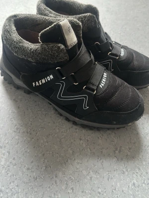 Svarta vinterkängor med fuskpäls - Säljer ett par svarta kängor med grå fuskpälsfoder och kardborreband. Yttermaterialet är textil och syntet, sulan är grovmönstrad för bra grepp. Perfekta för kalla dagar.