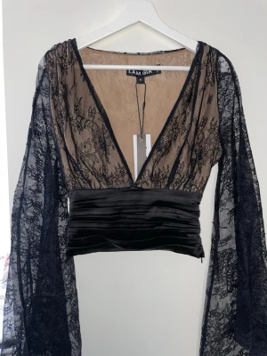 I AM GIA Svart spetsblus - Svart transparent spetsblus från I.AM.GIA med djup v-ringning och vida, utsvängda ärmar. Helt oanvänd pga felköp. Matchande kjol finns
