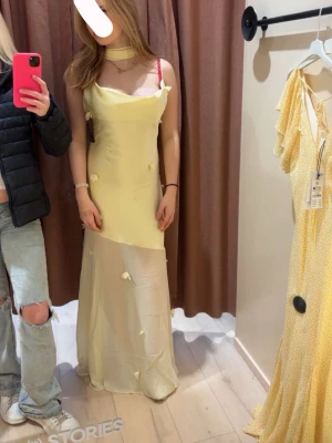Ljusgul långklänning från Gina - Superfin ljusgul långklänning från Gina tricot med asymmetrisk skärning och små blommiga detaljer. Klänningen har en scarf runt halsen och är med en elegant, flowy passform. Perfekt för sommarens alla tillfällen.
