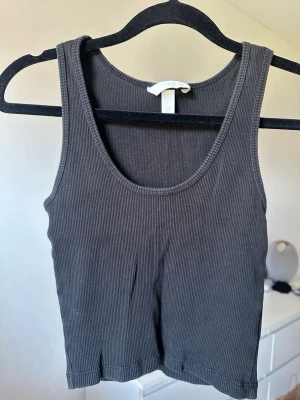 Mörkgrå ribbad linnetopp från H&M - Snygg mörkgrå ribbad linnetopp från H&M. Modellen är croppad med breda axelband och rund halsringning. 
