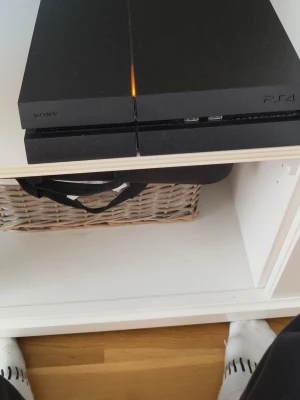 Sony PlayStation 4 med två spel - Säljer en svart PlayStation 4 från Sony med stilren, kantig design i plast. Konsolen har två USB-portar på framsidan och medföljer gör spelen EA Sports FC24 och FC25 till PS4. Perfekt för dig som vill ha en klassisk spelupplevelse med moderna sportspel.