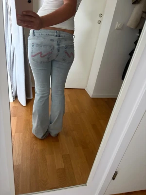 Ljusblå bootcut jeans  - Säljer ett par ljusblå bootcut jeans med slitna knän och broderade detaljer på bakfickorna. Jeansen har  låg midja. Storlek 36.