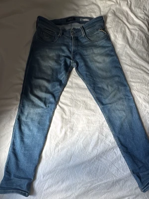 Replay Anbass - Säljer ett par blå slim fit jeans från Replay med snygga slitningar. Jeansen har en 32 midja och 30 längd. Jeansen har lite stretch för skön passform. De är använda men i bra skick. Priset är inte hugget i sten så det går att diskuteras. 