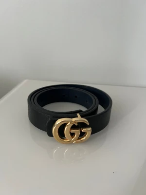 Svart skärp med GG-spänne från Gucci - Snyggt svart bälte från Gucci med det ikoniska dubbla GG-spännet i guld. Bältet är tillverkat i slätt skinn och har en klassisk, stilren design som passar till många olika outfits. Se skick på bild 
