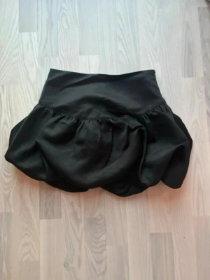 Svart voluminös kortkjol med dragkedja - Svart kortkjol med voluminös form och bred midja. Kjolen har en diskret dragkedja i sidan för enkel på- och avtagning. Perfekt för dig som vill ha en statement piece i garderoben. Pris går att diskutera 