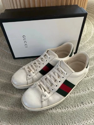 Gucci ace - Klassiska vita sneakers från Gucci i läder med de ikoniska gröna och röda sidoremsorna. Lågt skaft och vita snören. Perfekta för dig som vill ha en clean och lyxig look med streetvibe.