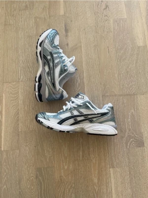 Asics silvriga sneakers med mesh - Snygga sneakers från Asics i silver, vitt och svart. Ovandelen är i mesh och syntet med coola detaljer och klassisk Asics-logga på sidan. Sulan är vit med svarta partier undertill och skon har vita skosnören. Perfekt för en sportig och trendig look.