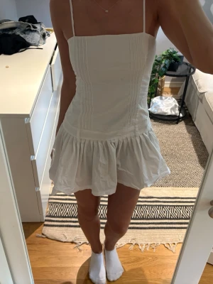 Vit kort klänning med volangkjol - Säljer en söt vit kort klänning med smala axelband och en volang underdel. Klänningen har sömdetaljer framtill och är perfekt för varma sommardagar💞🙏🏼