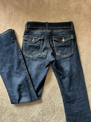 Jeans  - Lågmidjade bootcut jeans från Gina med knappfickor bak. 