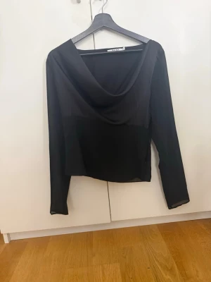 Svart långärmad topp från NA-KD - Svart långärmad blus från NA-KD med urringning och lätt transparent material nertill och i ärmarna. Snygg och stilren modell som passar perfekt till jeans eller kjol. Tunn och luftig känsla med en elegant touch.