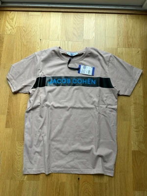 Jacob Cohën T-shirt  - Säljer nu denna helt nya Jacob Cohen T-shirten med tags kvar! En riktigt snygg beige färg med blå text, storlek L men sitter mer som en M! Nypris är någon tusenlapp! Skriv vid frågor 👌