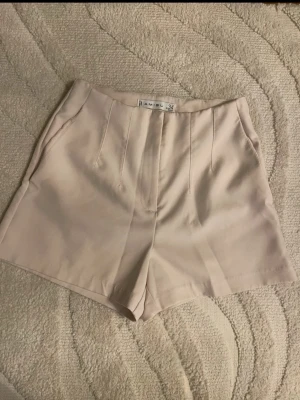 Beige högmidjade shorts från Amisu - Snygga beige shorts från Amisu med hög midja och stilrena sömdetaljer framtill. De har fickor på sidorna och är tillverkade i ett mjukt material som känns skönt mot huden. Perfekta för varma dagar och enkla att matcha med olika toppar.