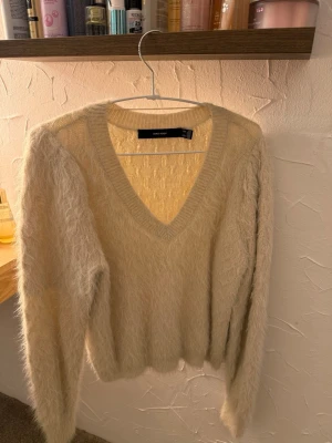 Beige fluffig stickad tröja V-ringad - Mysig beige stickad tröja från Vero Moda med fluffig textur och djup V-ringning. Långärmad modell med ribbade muddar och avslappnad passform. Perfekt för lager-på-lager och en chill look.