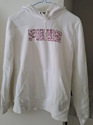 Vit hoodie från Puma med tryck - Snygg vit hoodie från Puma med rosavit mönstrad logga på bröstet. Perfekt för en avslappnad och sportig stil.
