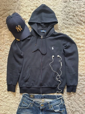 Ralph Lauren Zip-Up - Säljer denna skitsnygga Ralph Lauren zip up då den tyvärr inte används längre. Väldigt bra skick och ser nästan helt ny ut!   * Märke: Ralph Lauren * Storlek: S * Färg: Mörkblå * Skick: Väldigt bra kondition  Endast lite nopprig på ett litet ställe, annars finns det inga tecken på användning över huvudtaget. QR-kod finns att skanna för äkthetskontroll ✅  swag rap streetwear baggy vintage skate hiphop y2k affliction archive underground avant garde japan style OG 2000s flared washed affliction jea