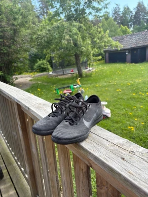 Svarta Nike sneakers med mesh - Snygga svarta Nike sneakers med lågt skaft och ventilerande meshmaterial. Skorna har en tydlig vit swoosh-logga på sidan och klassisk snörning. Perfekta för en sportig och stilren look.