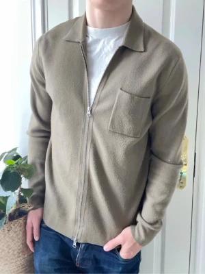Olivgrön overshirt från Samsoe - Stilren olivgrön overshirt från Samsoe Samsoe med rak passform, dragkedja framtill och en bröstficka. Tillverkad i ett mjukt, strukturerat material som ger en avslappnad men snygg look. Perfekt att bära över en t-shirt eller skjorta.
