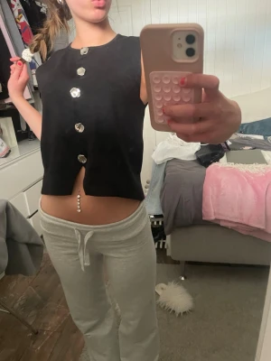 Svart ärmlös topp med stora knappar - Svart ärmlös topp med stora, silvriga knappar framtill. Toppen är croppad och har en rak passform. Perfekt för dig som gillar en stilren och trendig look.