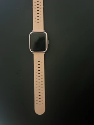Beige smartklocka med silikonarmband - Stilren smartklocka med fyrkantig display och beige silikonarmband. Klockan har en modern design med metallram runt skärmen och justerbart armband. Perfekt för dig som vill ha koll på notiser och hälsa direkt på handleden.
